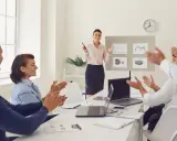 Uśmiechnięta kobieta kończy prezentację po angielsku. Zespół klaszcze, doceniając jej pracę.