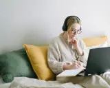 Dziewczyna w słuchawkach pisze w notatniku, szukając zwrotów do opinion essay.
