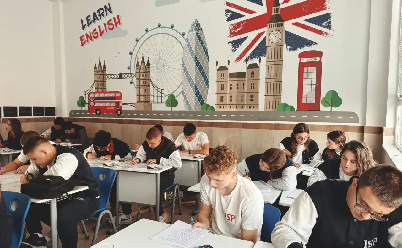 Uczniowie piszą egzamin B2 z angielskiego w sali lekcyjnej ozdobionej motywami Londynu.