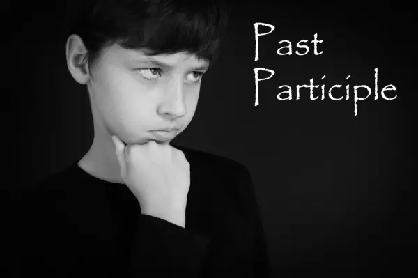 Chłopiec zamyślony, z podpartą brodą, jakby zastanawiał się nad trudnym zadaniem, być może nad gramatyką i formą **czas past participle**.